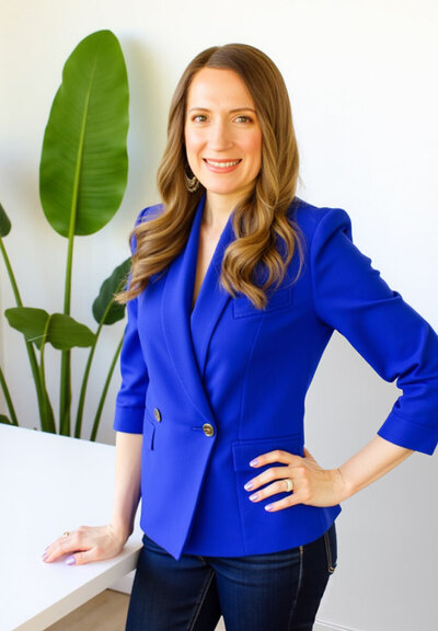 Stacey from Xanthe Bookkeeping smiling in a cobalt blue blazer, standing with her hand on her hip in front of a Birds of Paradise plant.