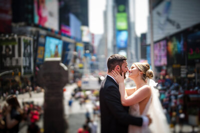 A wedding couple kissing while standing in the middle of  a busy city.