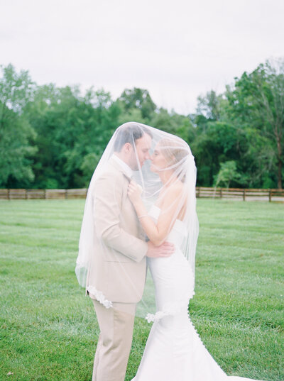 Groom standing behind bride while both look down smiling