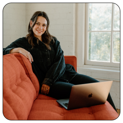 Portrait of Emma Leigh Studios' owner and principal designer, sitting on red sofa.