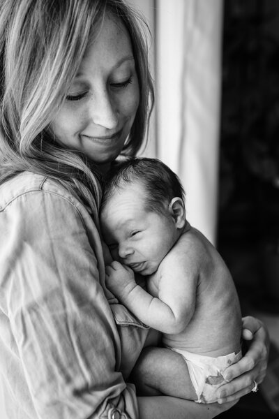 A black and white image of a woman gently holding a newborn baby close to her chest, both sharing a peaceful moment with soft expressions.