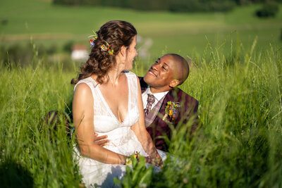 Ein verliebtes Brautpaar liegt Hand in Hand in einer blühenden Wiese und tauscht zärtliche Blicke aus. Ein romantischer Moment in der Natur.