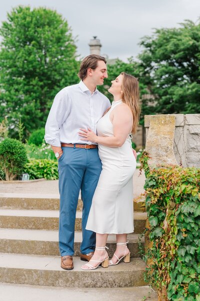 A man and woman standing on the steps in the garden at Eolia Mansion, peering at one another.