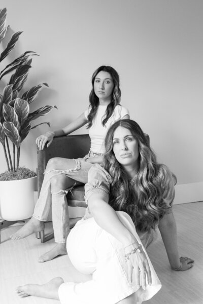 one woman sitting in a chair while another woman sits on the floor with a plant in the background