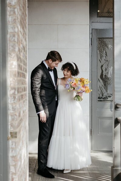 A bride and groom sharing a quiet moment on a porch, with the bride holding a pastel-colored bouquet.