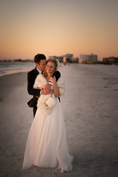 groom embracing bride while standing on the beach