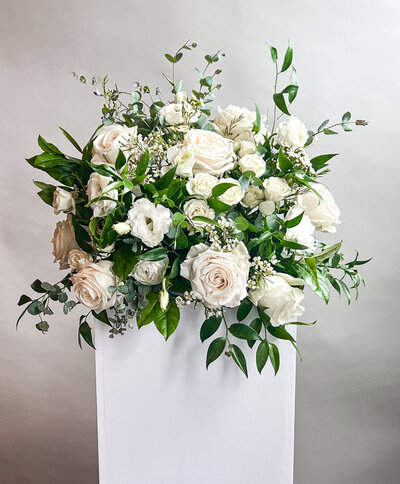 Large floral arrangement of white flowers with greenery on a white block