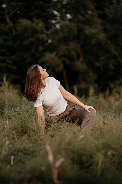 Tessa Adrian führt eine fließende Yoga-Pose auf einem Feld aus, verbunden mit der Natur.
