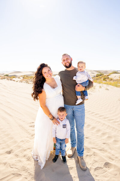 Cute family with two smaller children smiling for the camera at the beautiful sand dunes in Utah!