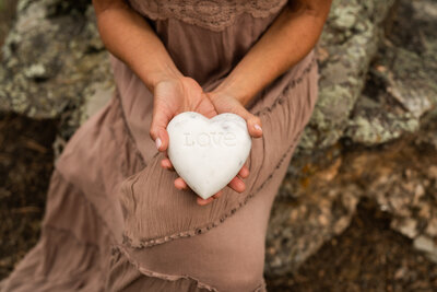 Katheryn sitting outside holding a stone with the word "love" carved into it