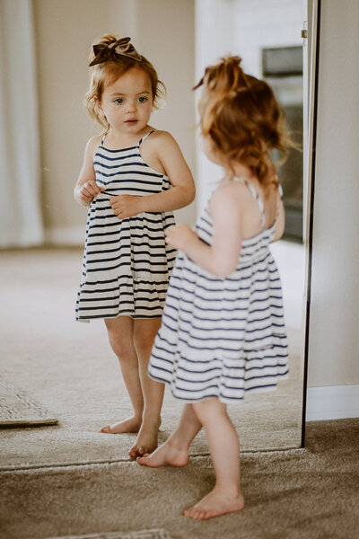 oyung girl in stripped dress looking at herself in mirror