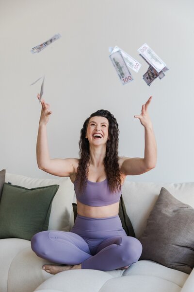 Hailey Ann Co Bookkeeper and somatic Money Coach for female entrepreneurs professional headshot of Hailey throwing money into the air 
