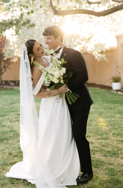 Romantic golden hour portrait of luxury bride and groom laughing in the sun holding a white bridal bouquet at Villa Parker