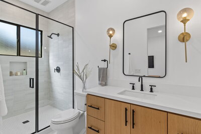 Renovated bathroom featuring a frameless glass shower with matte black fixtures, wood vanity, and gold accent lighting—completed by AW Development Co. for a Los Angeles investment property.