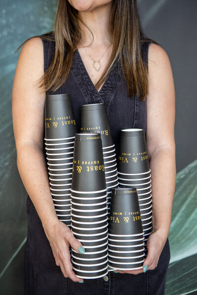 Woman in dress holding stacks of coffee cups