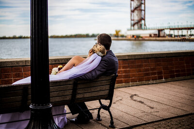 Bride and groom snuggle on a bench with the Bicentennial Tower in the background in downtown Erie