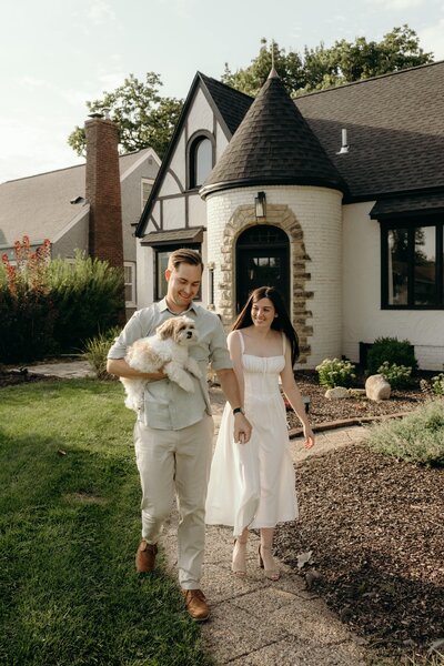 A newly engaged couple walks hand in hand down the sidewalk in front of their charing suburban home.