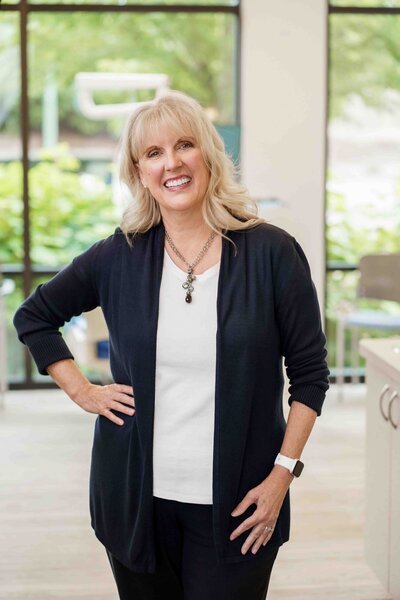 Orthodontic office receptionist stands for headshot smiling in their office wearing comfortable business cardigan during branding photoshoot