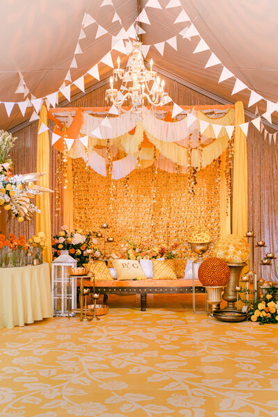 orange themed sikh wedding reception with a yellow couch place under white ceiling ribbons