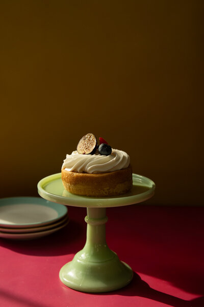 Lemon cake with fruit on green cake stand with side plates. 