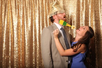 Couple in photobooth with lampshade prop on head and champagne prop