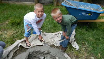 two boys smiling at the camera while building a fire pit in the backyard.