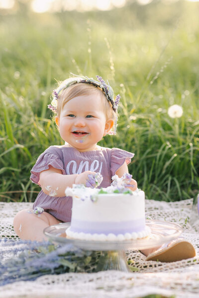 Little girl wearing a purple romper eating cake for the first time in Guyton, Ga