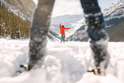 This joyful photograph captures a fiancé dancing on the frozen Lake Louise, with the fiancée gazing at her with happiness. The stunning winter landscape, with the iconic Chateau Lake Louise behind us, adds to the playful and romantic atmosphere of their engagement shoot.