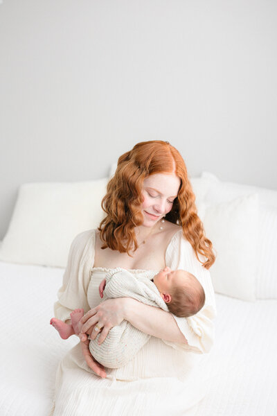 New mom wearing a cream Nothing Fits But dress holding her newborn baby boy  in a timeless northern kentucky newborn photography studio