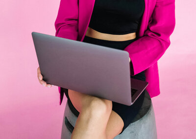 Trabajando en laptop con blazer fuchsia y fondo rosado.