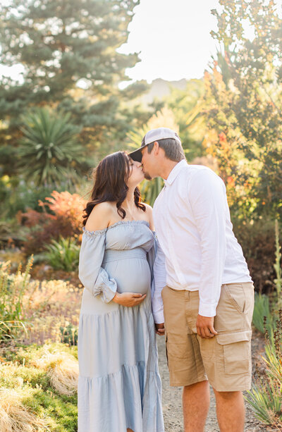 mom and dad kissing while mom holds baby bump for maternity photos in southern utah