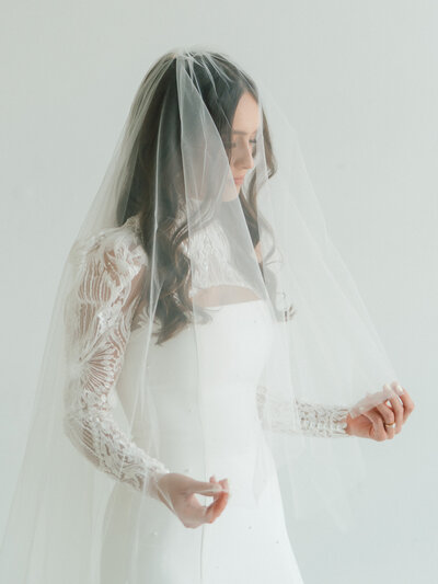 Portrait of bride sitting on a window sill holding a colorful bouquet and looking out the window