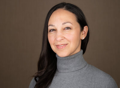 Woman poses in front of a brown background for her headshot session.