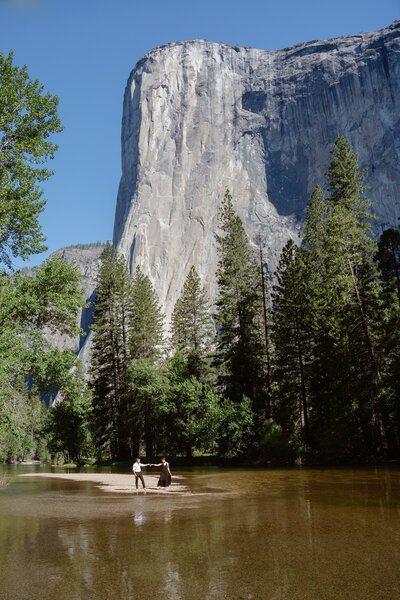 A couple hold hands in front of El Capitan in Yosemite National Park surrounded by water