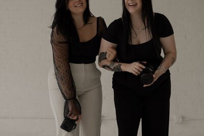 photo of two women linking arms and laughing together with cameras in their hands