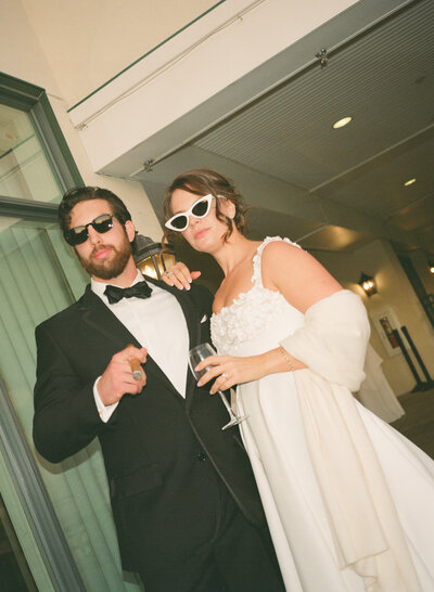 Film photo of bride and groom in sunglasses and holding their signature drink at a golf club in San Diego, California.