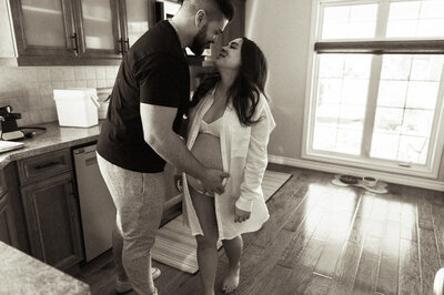 An expecting couple standing in the kitchen kissing documented by a Sudbury Documentary Photographer
