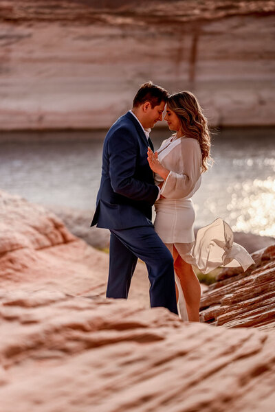 A couple embracing after an early morning engagement proposal, with the tranquil waters of Lake Powell and the soft light of dawn.
