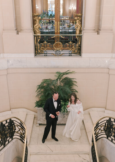 A bride and groom stand at the top of the stairs at the Perry Belmont House welcoming their guests