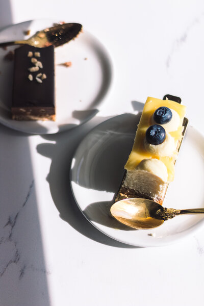 Plated lemon blueberry dessert and chocolate slice with golden spoons served at Gold Leaf Pastries in Kamloops BC.