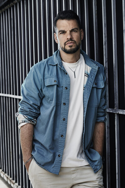 Casual portrait of David Victori in a denim jacket, standing against a modern striped background, exuding confidence, captured by Ylva Erevall.