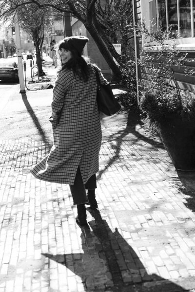 A woman smiles while looking over her shoulder and walking away. 