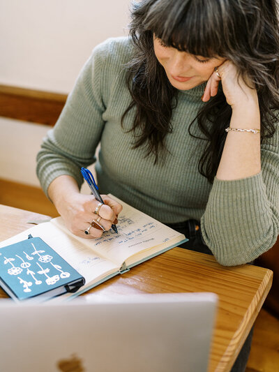 Bloem Creations founder Carrie writes in a notebook, representing her offering of copywriting services for small biz owners. 