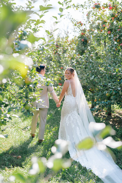A couple holding hands walking through an apple orchard on their wedding day in Cape May, New Jersey.