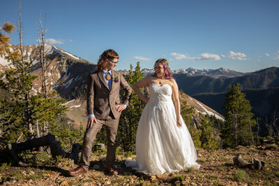Bride & Groom stand on a mountain ridge with hands on hips looking at each other -- this desolate spot is where they chose to have their helicopter elopement here in Montana.