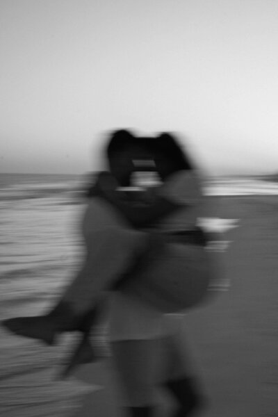 Blurred black and white photo of couple on the beach. the man caring the woman