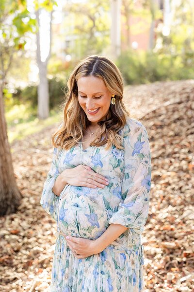 woman in floral dress holds baby bump for maternity pictures in LA