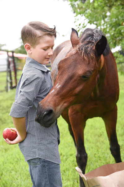 boy holding an apple behind his back while his brown pony tries to reach around him to get the apple