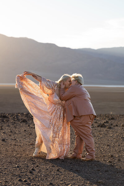 A queer couple kisses as one woman tosses her sparkly dress in the air