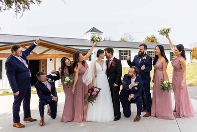 bride and groom nuzzle noses in front of their venue as their wedding party cheer for them on their wedding day